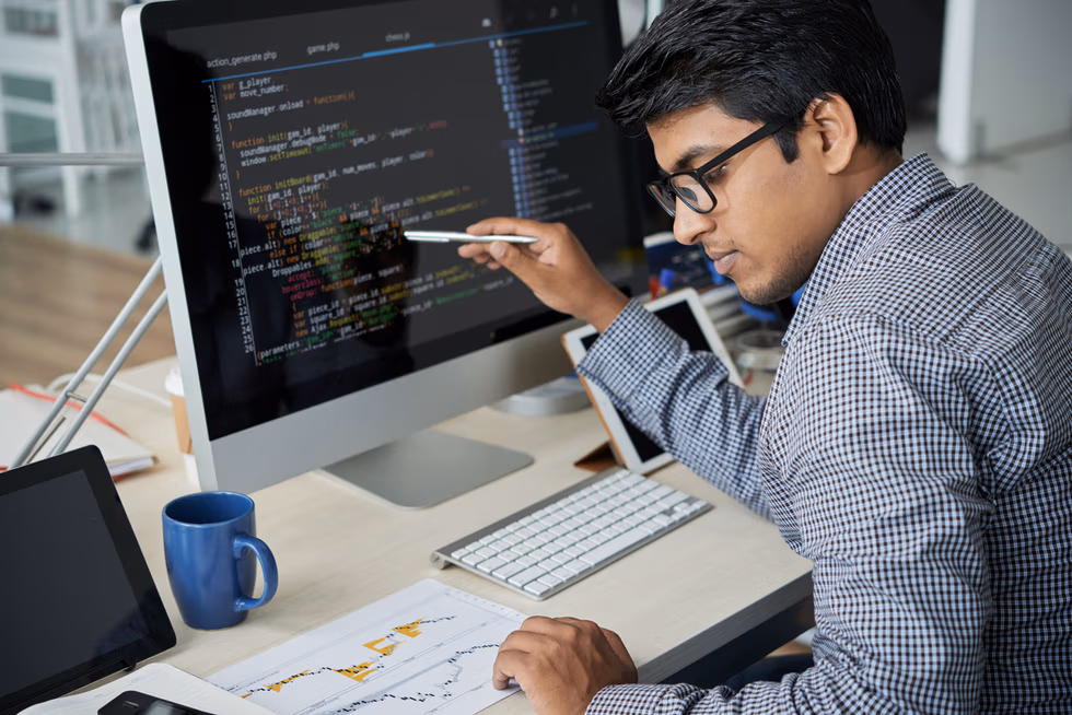 Indian programmer in eyeglasses pointing at computer monitor and checking the statistics of website