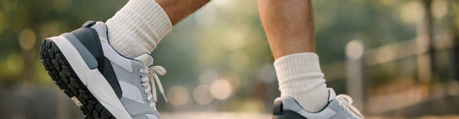 Outdoor lifestyle photograph of a person walking comfortably in a park or city street, premium socks with sneakers visible, natural daylight, calm wellness atmosphere, realistic movement