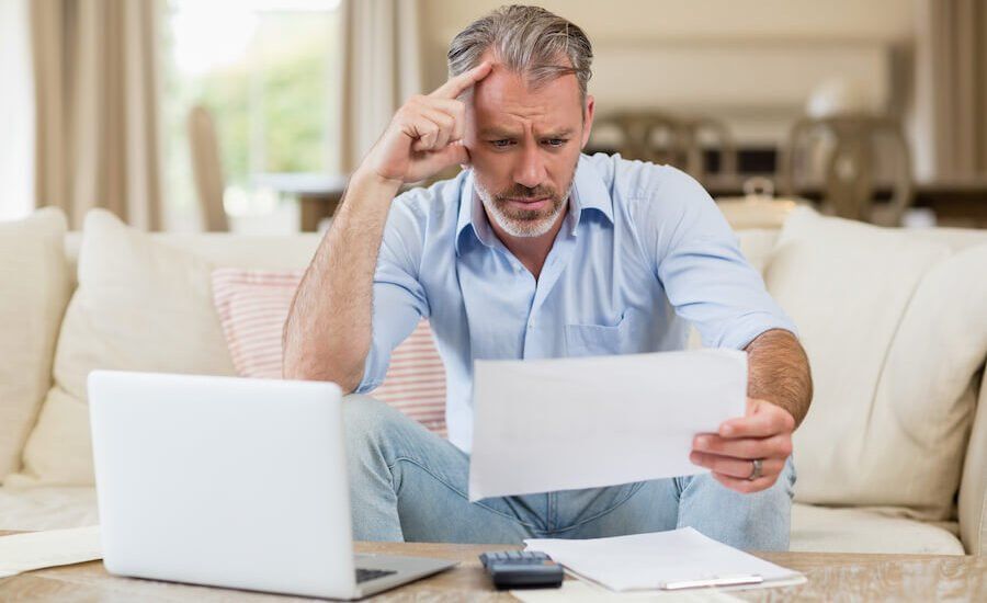 A man sitting on a couch with a laptop and paper, possibly discussing debt settlement in UAE or a debt settlement loan.