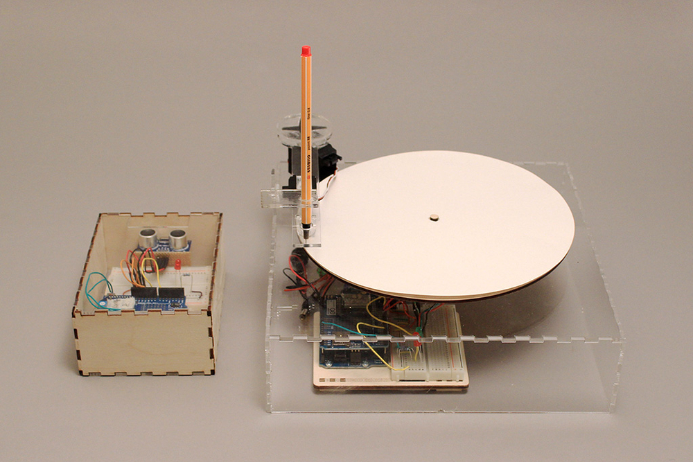 A photo of two machines, the smaller has electronics inside and a sensor, the larger has a large disc and drawing pen