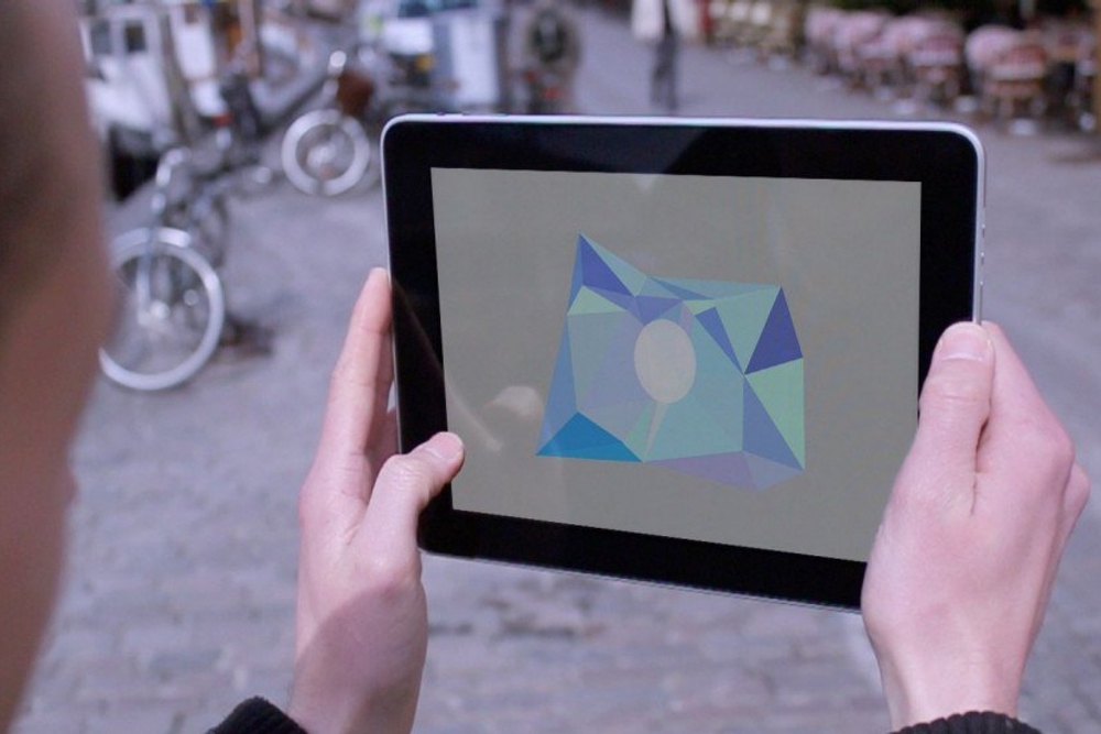 Looking over the shoulder of someone holding a tablet in a street, on the screen are some triangles clustered together