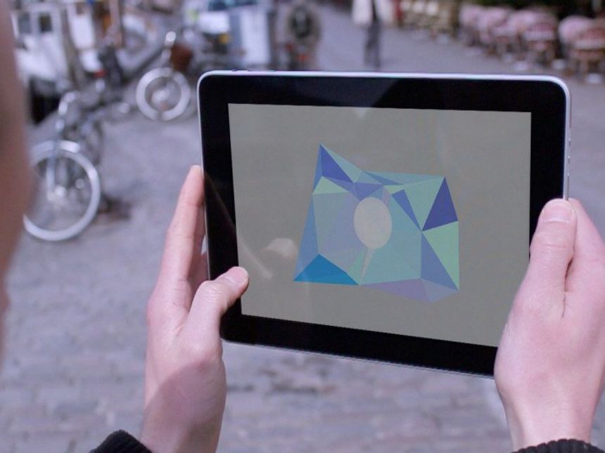 Looking over the shoulder of someone holding a tablet in a street, on the screen are some triangles clustered together