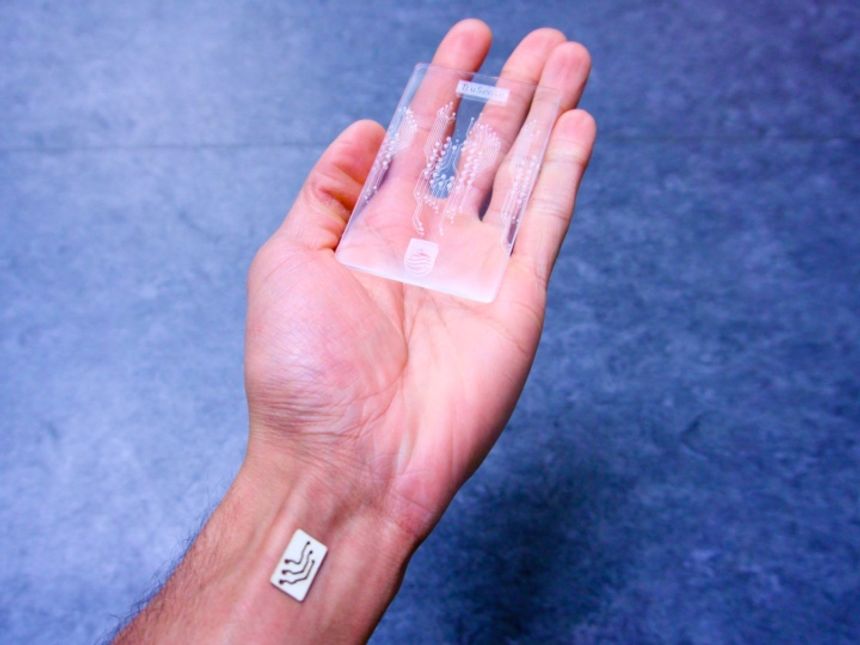 A photo of someones hand holding a transparent card with a microchip stuck to their wrist
