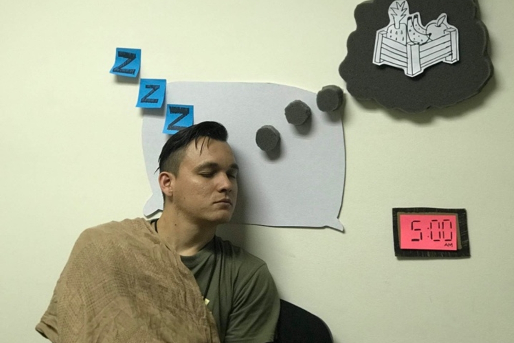 A photograph of someone pretending to sleep, with speech bubbles and 'z' hand draw and stuck around their head