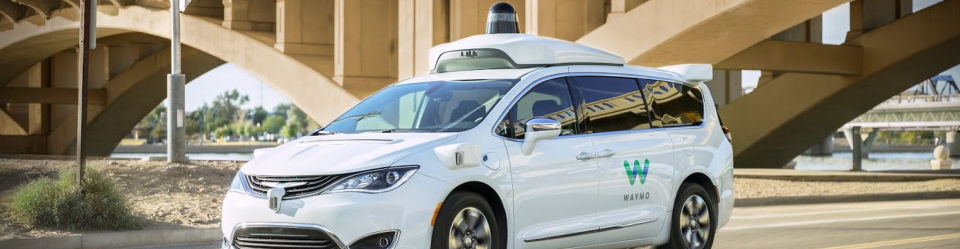 A white Self-driving Waymo car driving on the highway just passed a bridge.