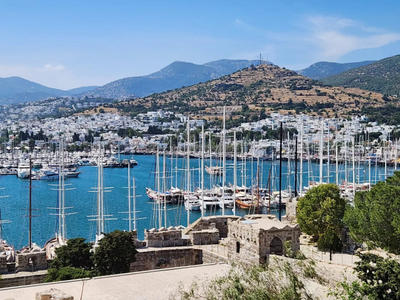 View of a marina filled with sailboats and yachts with hills and white buildings in the background