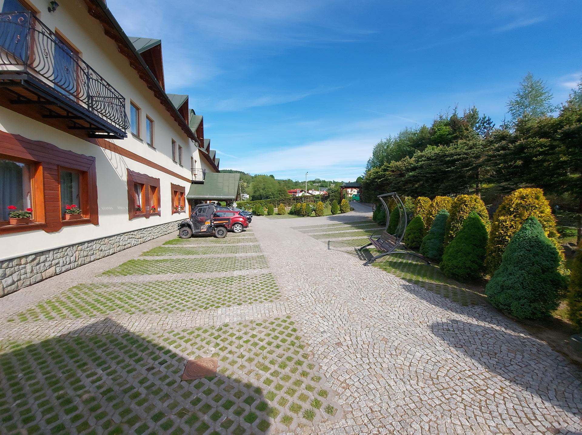 Parking Hotelu Piastun w Krynicy-Zdroju – widok na budynek i miejsca postojowe.