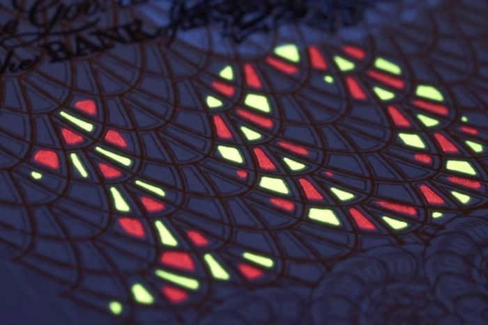 Close-up of a UK banknote under UV light showing red and yellow anti-counterfeit security markers, a key example of the uses of europium in document authentication