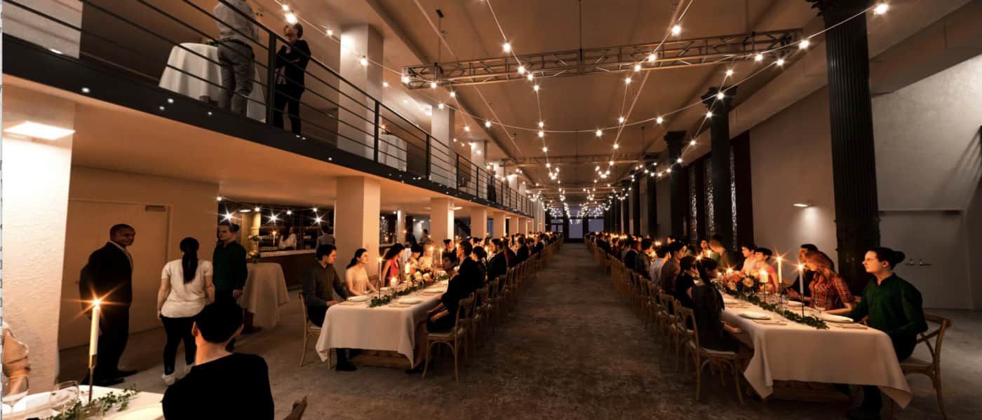 A long dining hall with string lights, crowded tables, and people enjoying a formal dinner event.