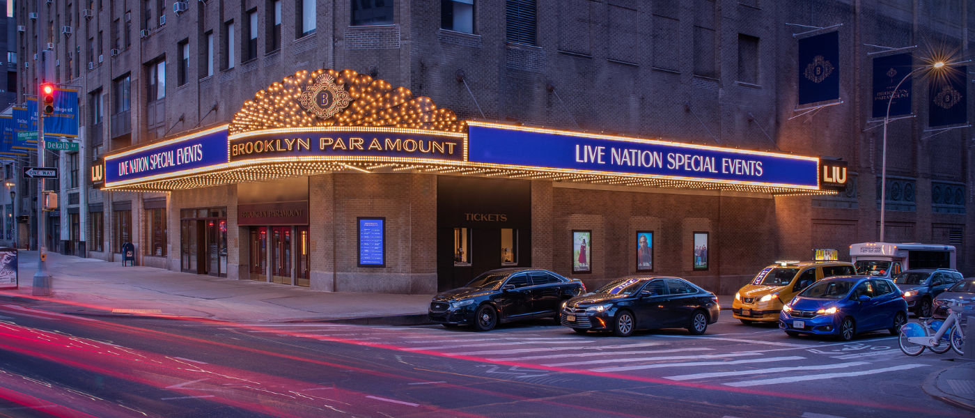 Brooklyn Paramount marquee lit up at night, cars parked in front, and blurred lights from passing traffic.