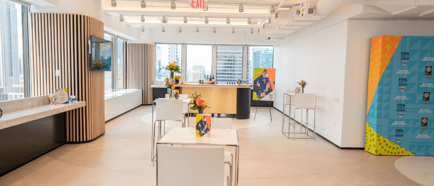 Modern, bright lounge with tall windows, white furniture, flowers, and views of city skyscrapers.