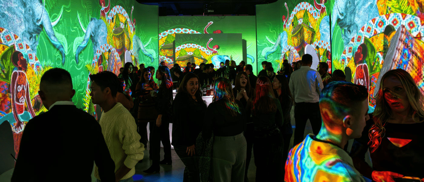 People at an art exhibit with bright, colorful, animal-themed digital projections on the walls and faces.
