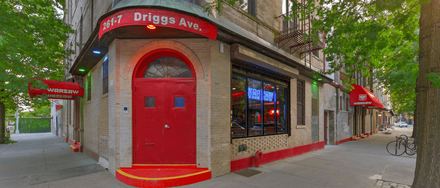 Corner building with a red door and awnings, labeled "Driggs Ave," in a tree-lined urban street.