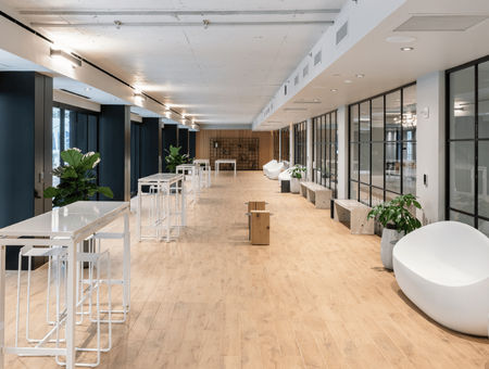 Modern open office space with large windows, white furniture, wood floor, and glass-walled meeting rooms.