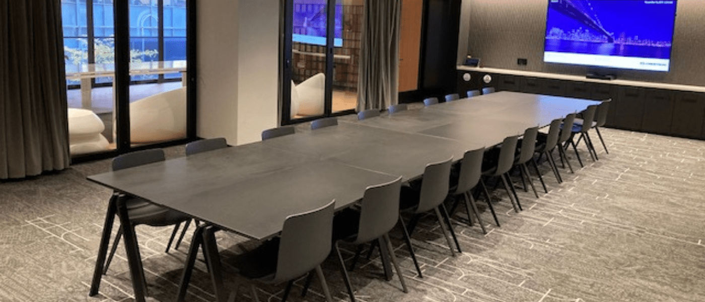 A modern conference room with a long black table, many chairs, and a large screen on the wall.