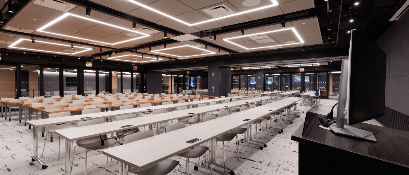 Modern conference room with long tables, rows of chairs, large windows, and a podium at the front.