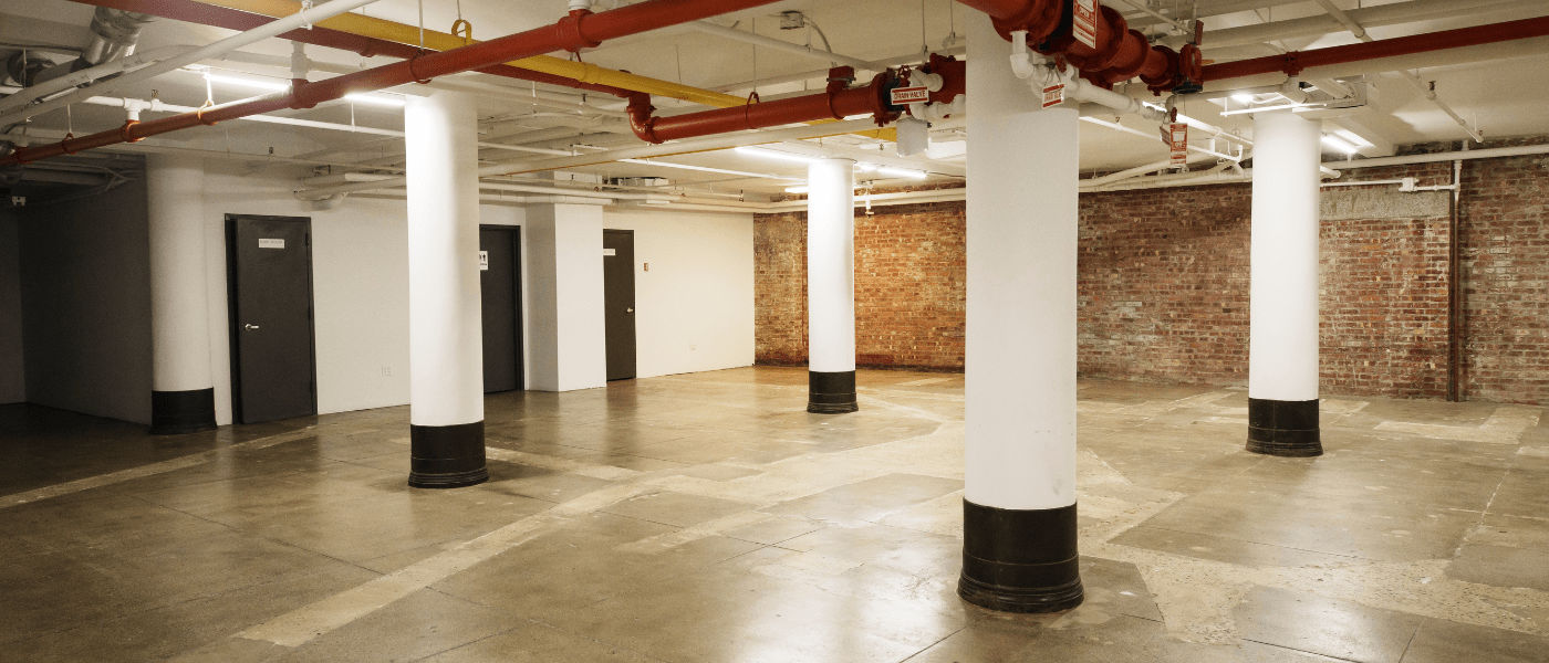 Spacious basement with concrete floor, white columns, exposed pipes, and brick walls.
