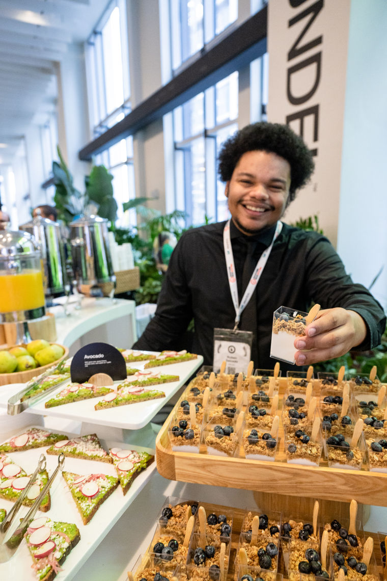 Smiling person serves parfait at a buffet with avocado toast and granola cups at a bright indoor event.
