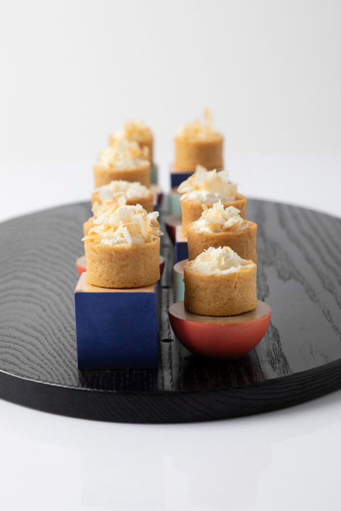 Small round savory pastries topped with shredded cheese on colorful geometric blocks on a black wooden platter.