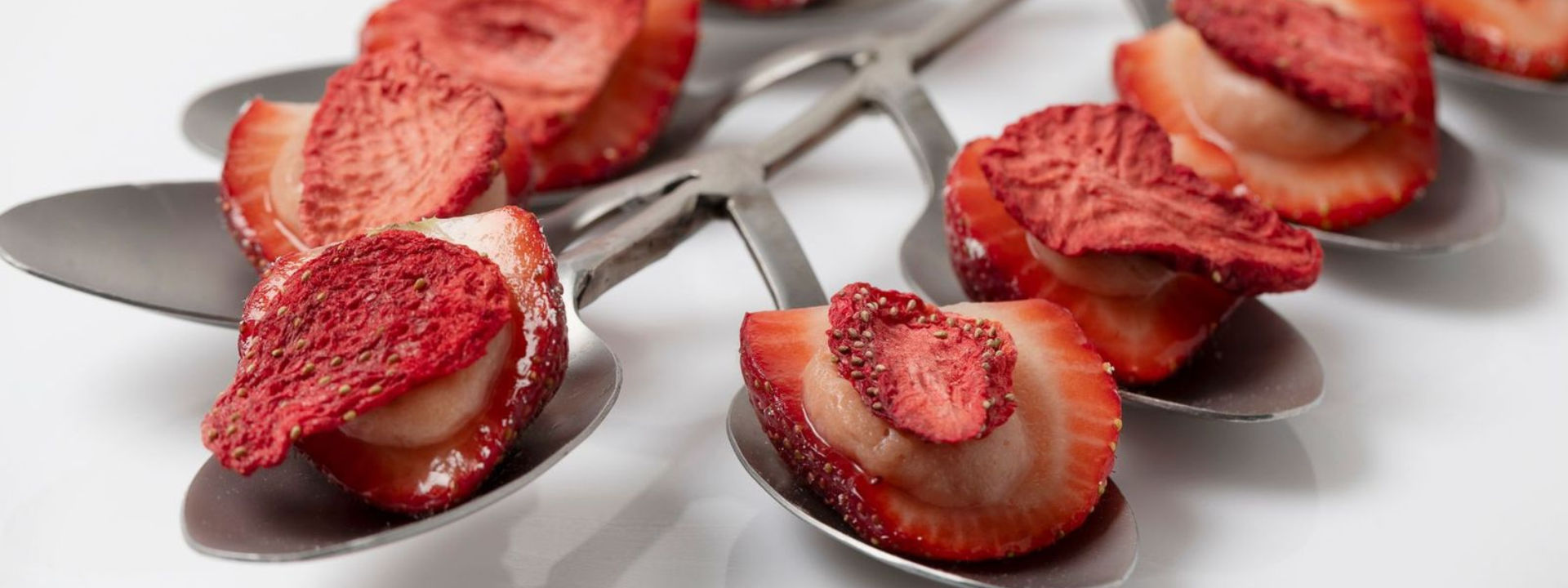 Spoons holding sliced fresh and dried strawberries arranged in a neat, artistic display on a white surface.