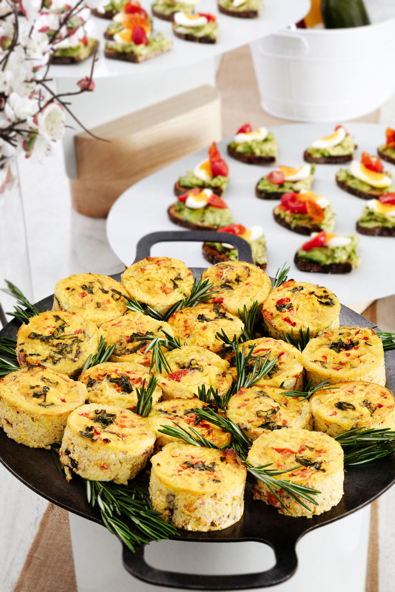 Mini frittatas garnished with rosemary on a platter, with assorted canapés displayed in the background.