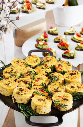 Mini frittatas garnished with rosemary on a platter, with assorted canapés displayed in the background.