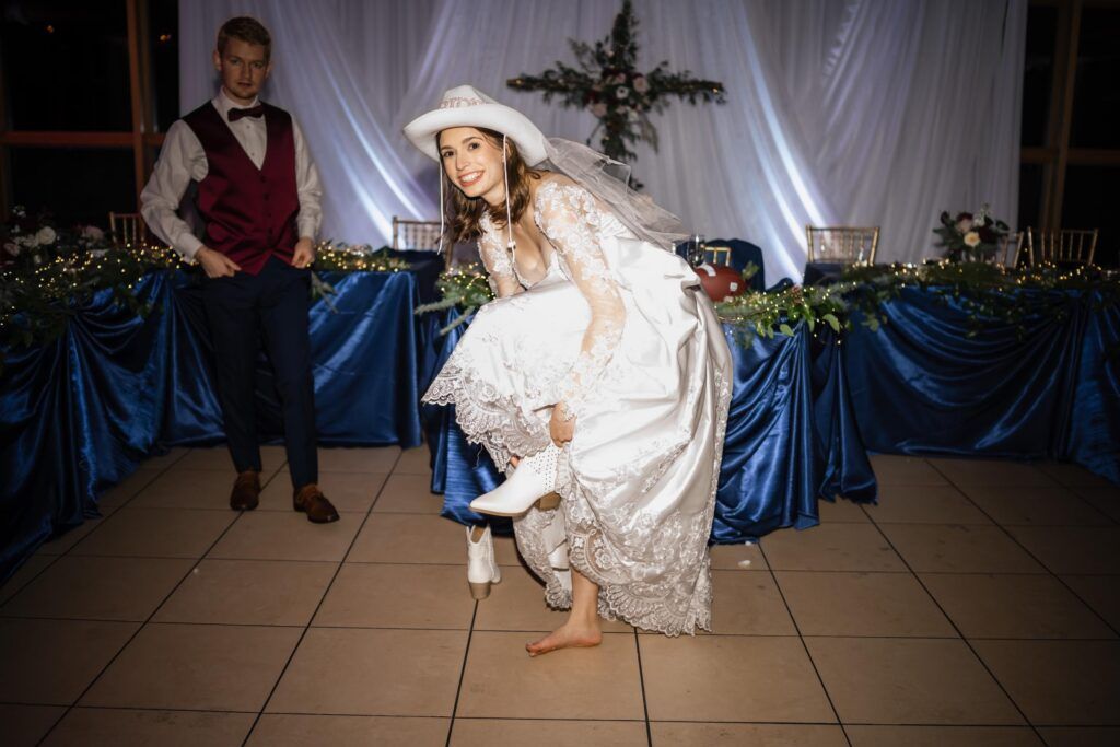 Bride with cowboy hat putting on her cowboy boots.