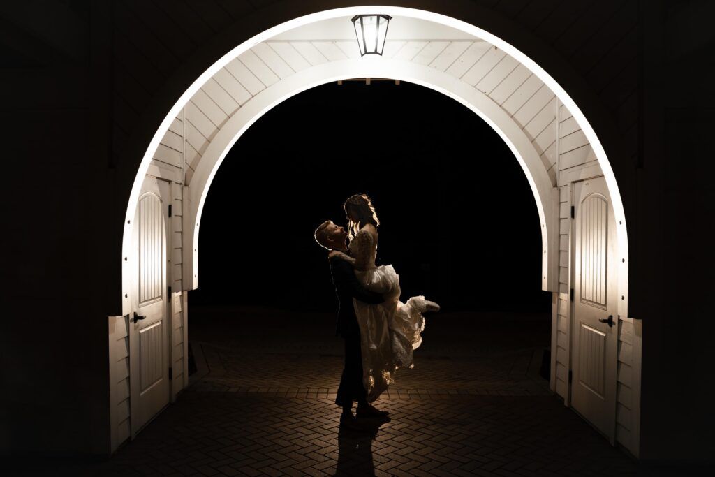 Newlyweds embrace, groom lifting bride in a tunnel.
