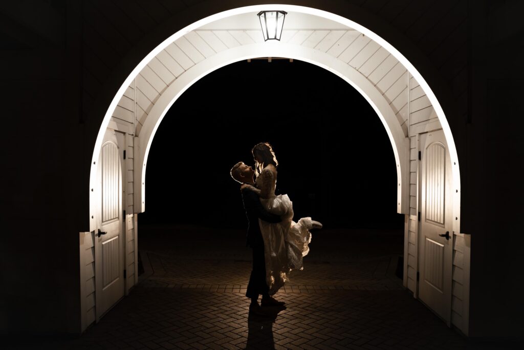 Newlyweds embrace, groom lifting bride in a tunnel.