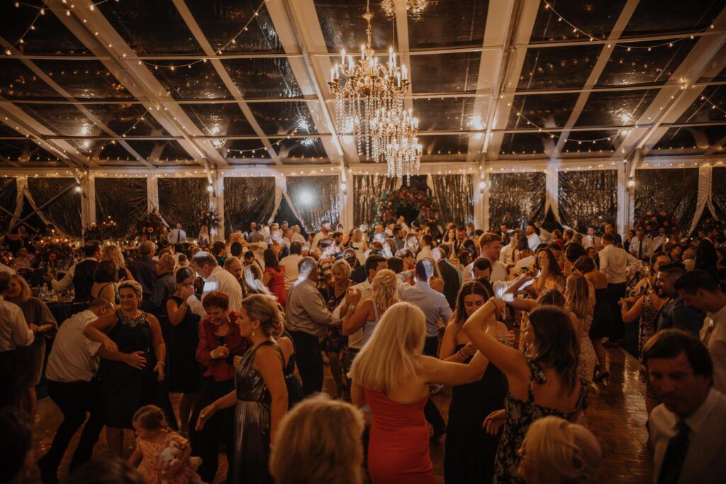Guests dancing at reception under clear tent and glowing lights.