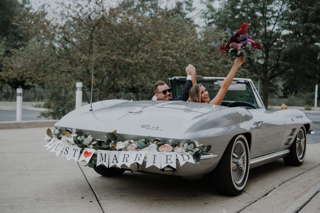 Newlyweds driving way in their vintage car.