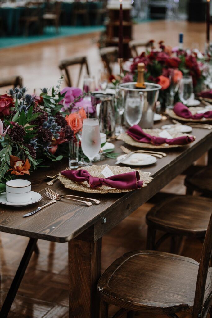 Receptions wood table, gold chargers and napkins with lush low centerpiece.