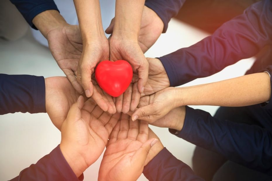 multiple hands coming together to hold a heart