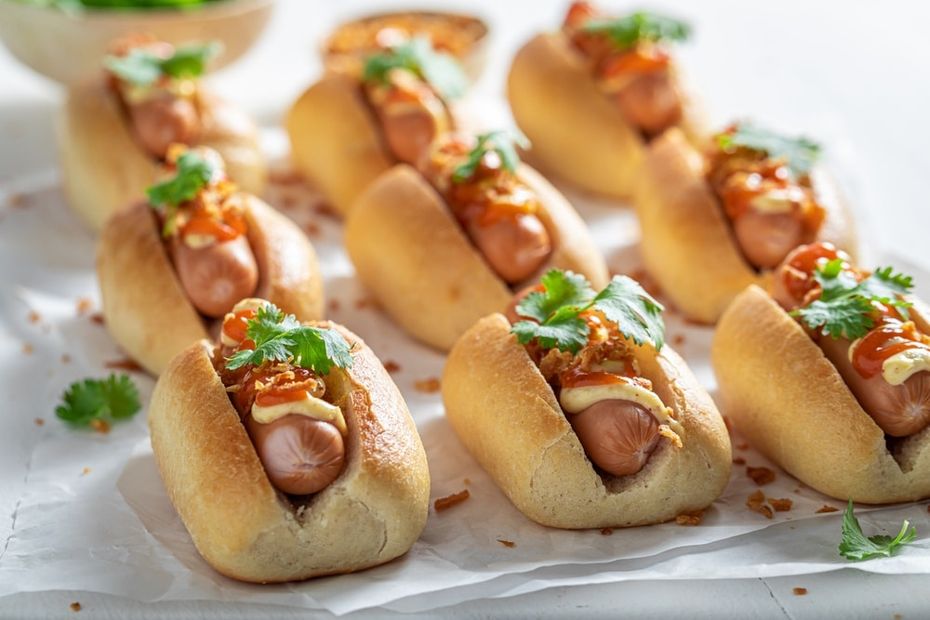 Mini hot dogs in buns with condiments on top