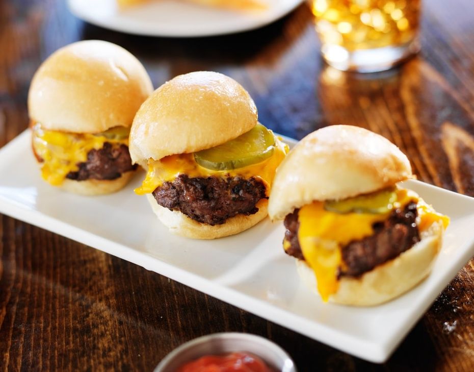 Three cheeseburger sliders on a white serving platter