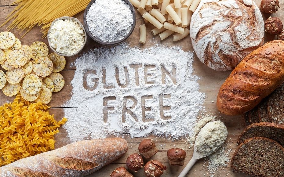 Gluten Free written in flour on a cutting board surrounded by gluten food