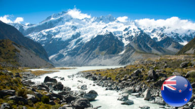 A river flows through a rocky valley with snow-capped mountains in the background under a clear blue sky. A small circular icon with the New Zealand flag is in the lower right corner, promoting บริการขอวีซ่า for your next adventure.