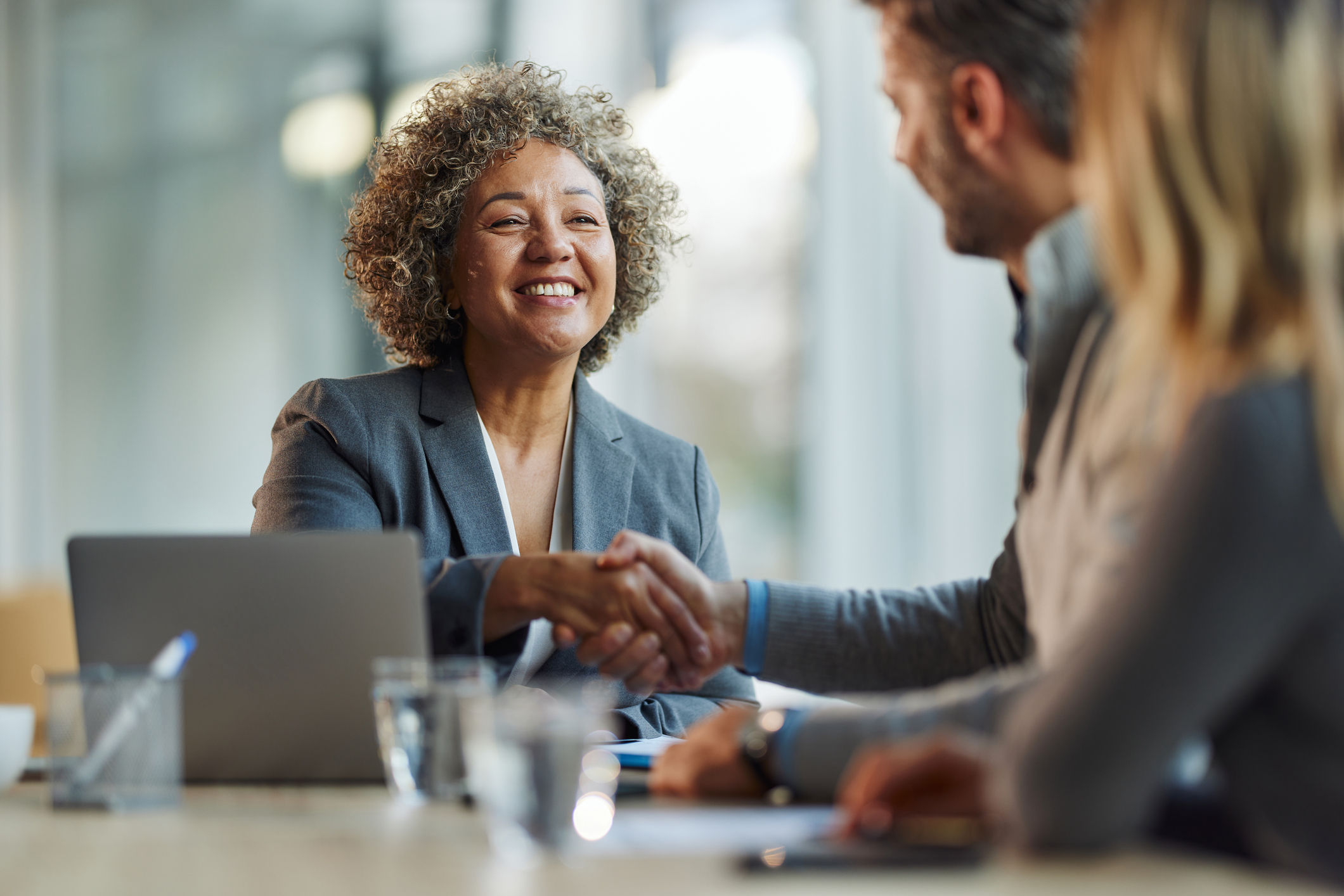 Mature business woman sitting down smiling and shaking hands with a man.