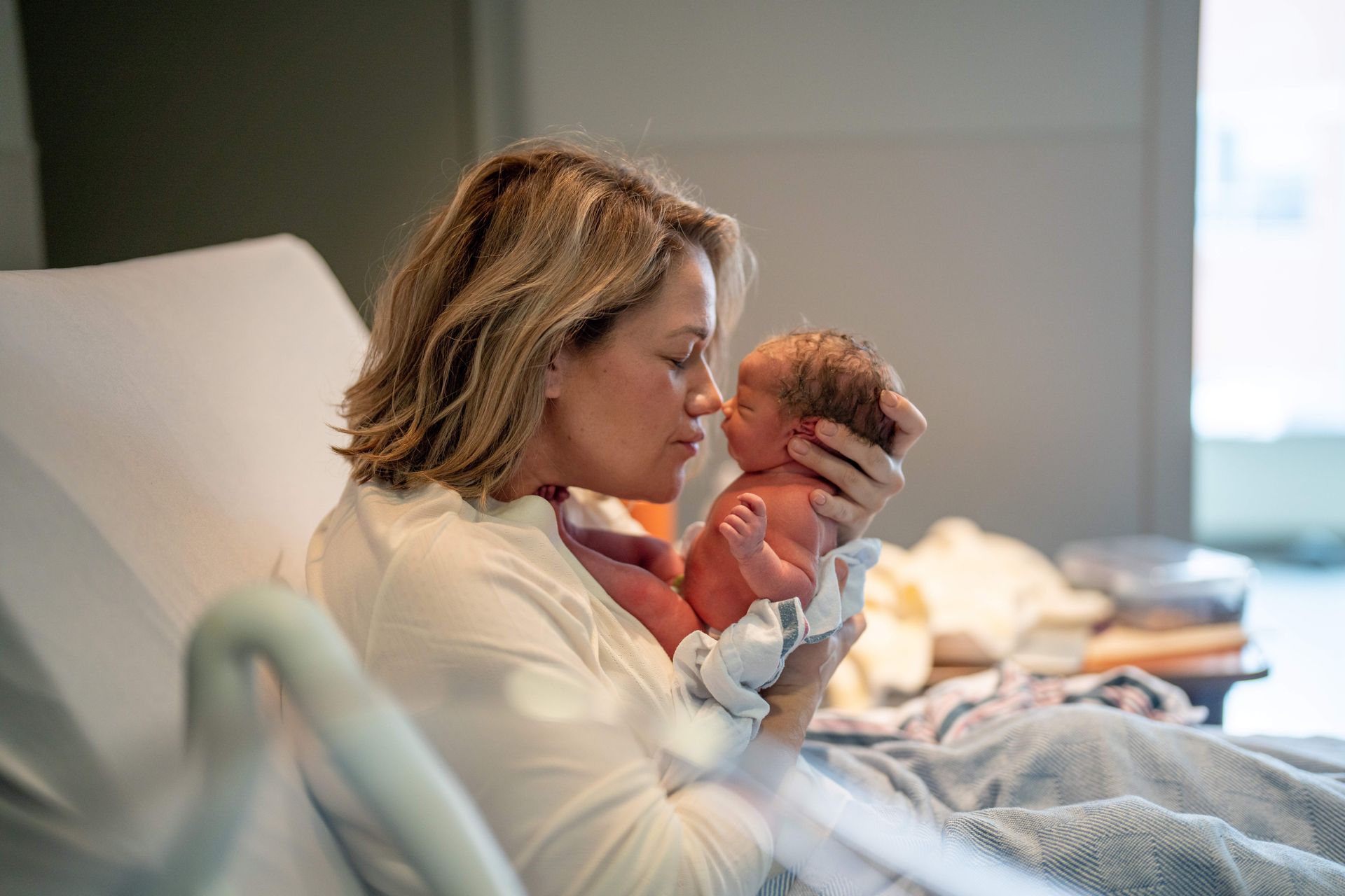 White woman in hospital bed touching noses with her newborn.