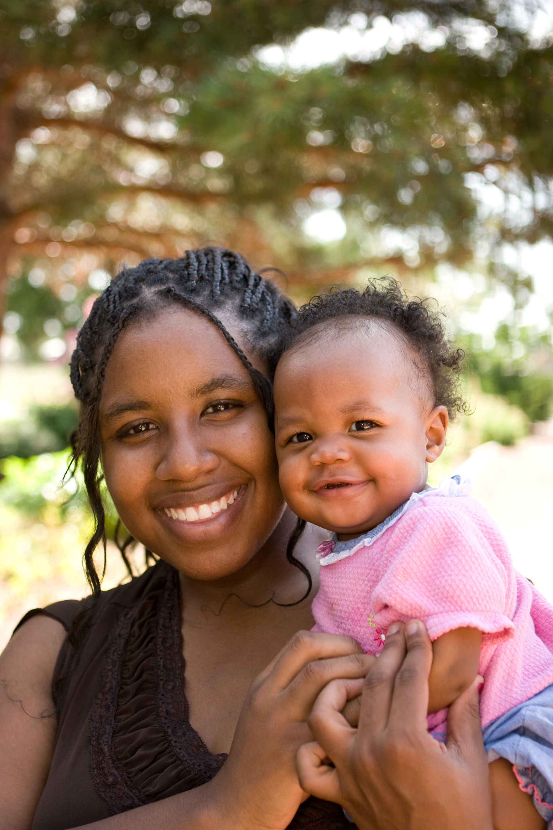 Black woman holding her baby outside, both are smiling.