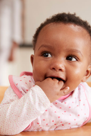 Black baby looking off to the side with her hand in her mouth.