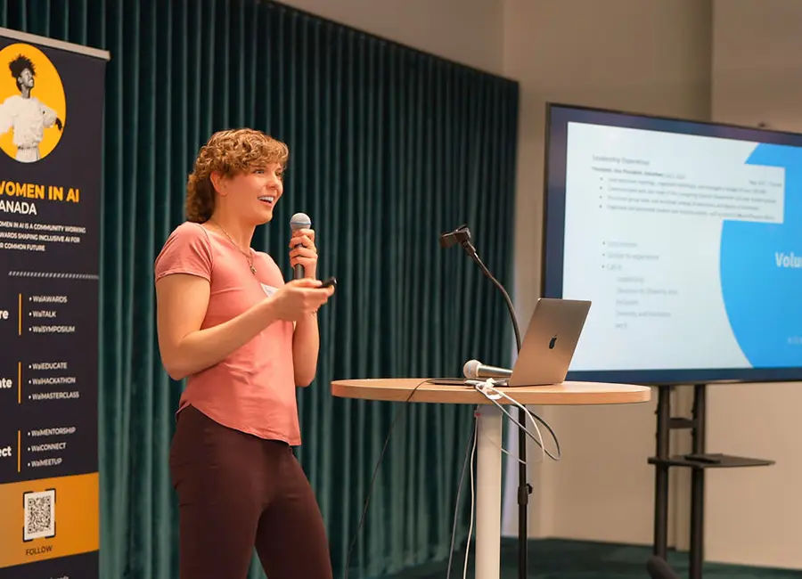 Mandy standing talking into a mic with presentation slides behind her