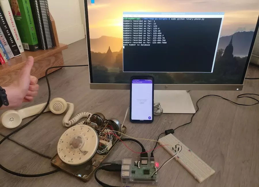 An old rotary phone with wires sticking out of it connected to a raspberry pi and monitor displaying text