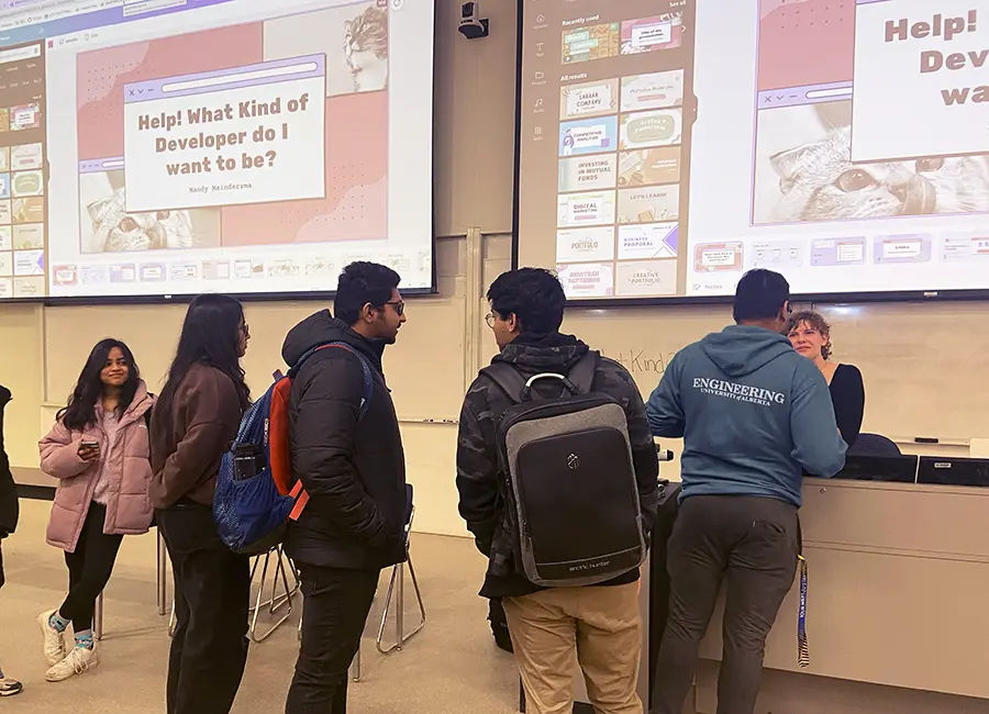 Mandy standing at the front of a large lecture hall with 10 student lining up to talk to her