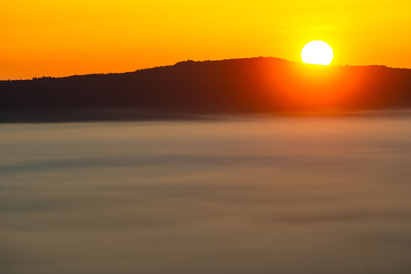 Een ondergaande zon beschijnt een laag wolkendek. © Billy Herman