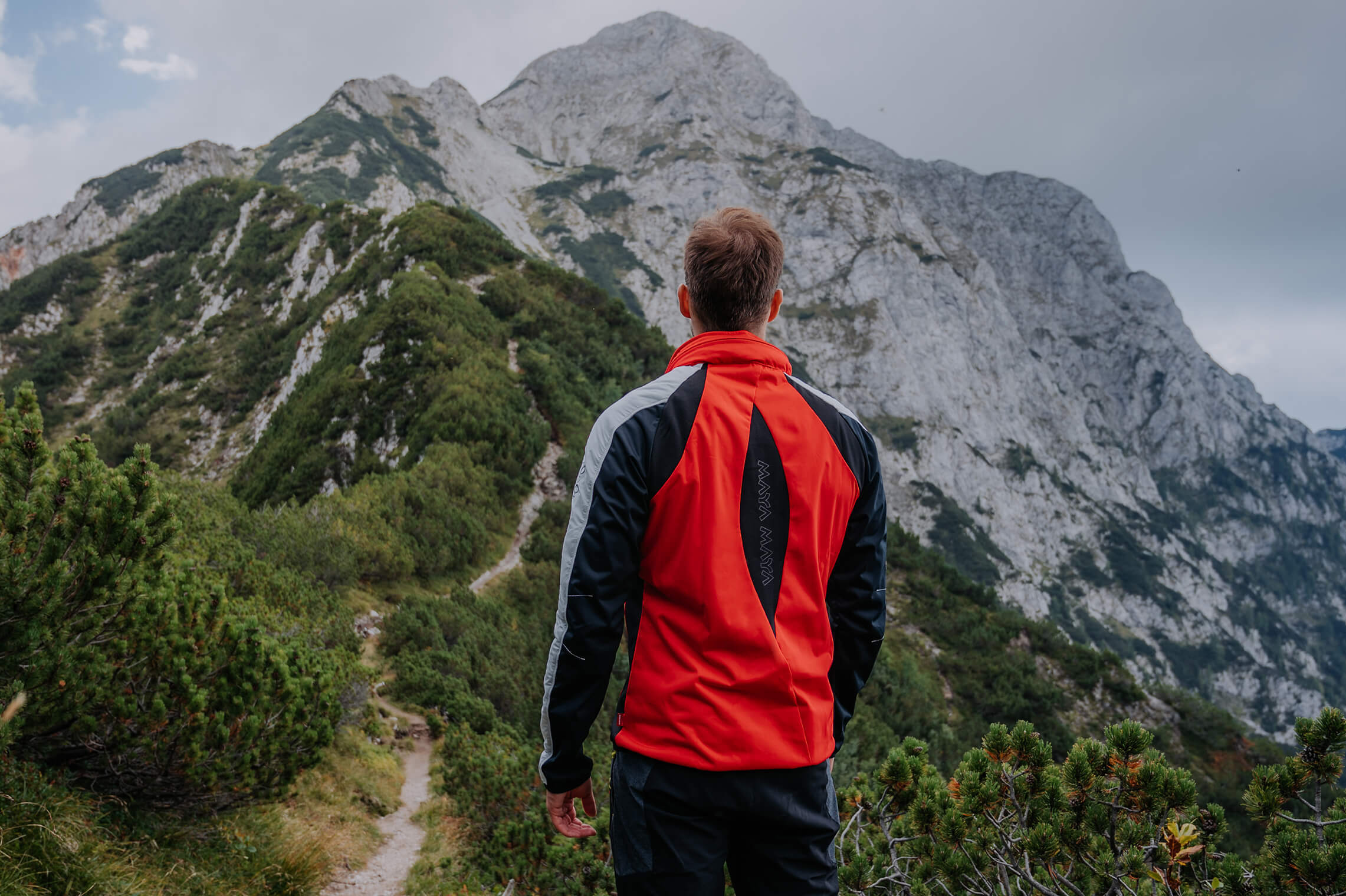 A man hiking on a mountain wearing a sports red softshell Themba jacket.