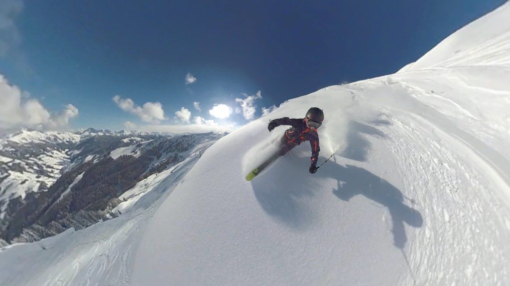 A guy freeride skiing down a snowy mountain on a sunny day.