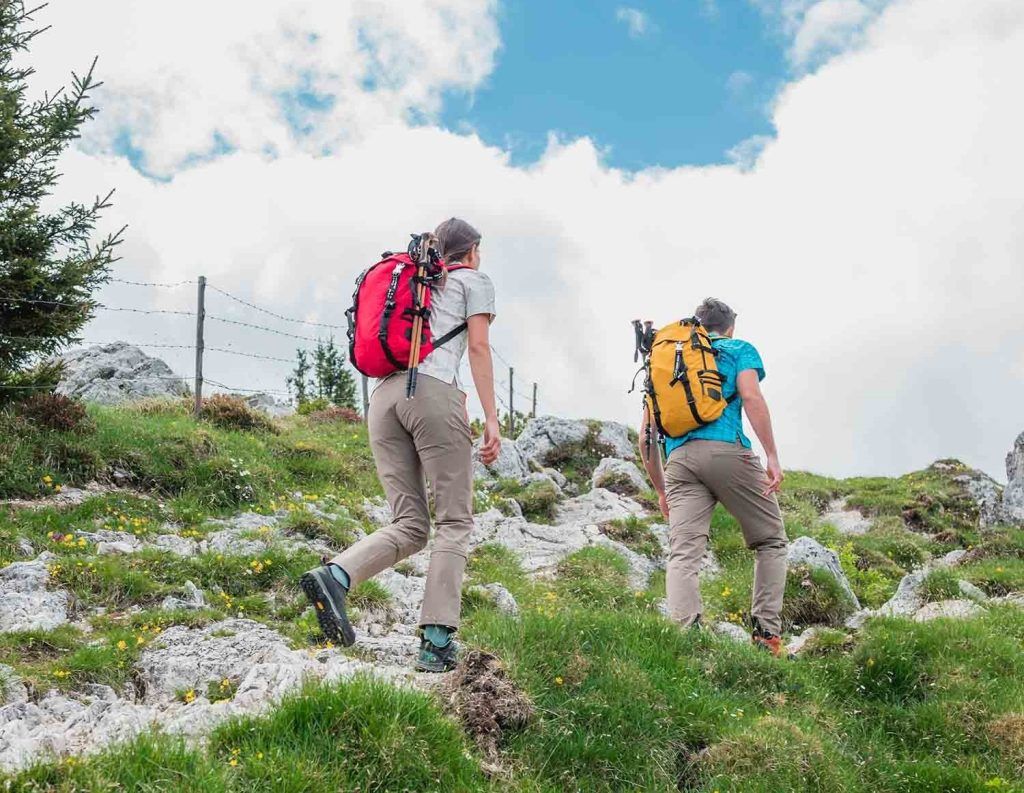 A man and a woman hiking up a mountain in outdoor luxury apparel in spring or summer.