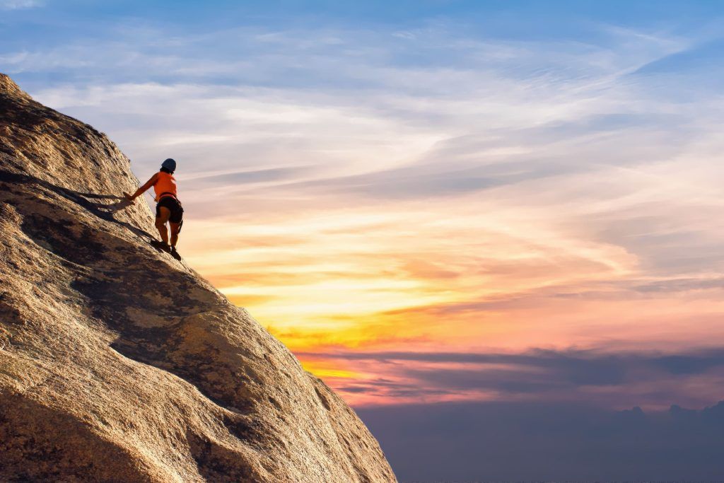 A woman rock climbing on a rock in the sunset.