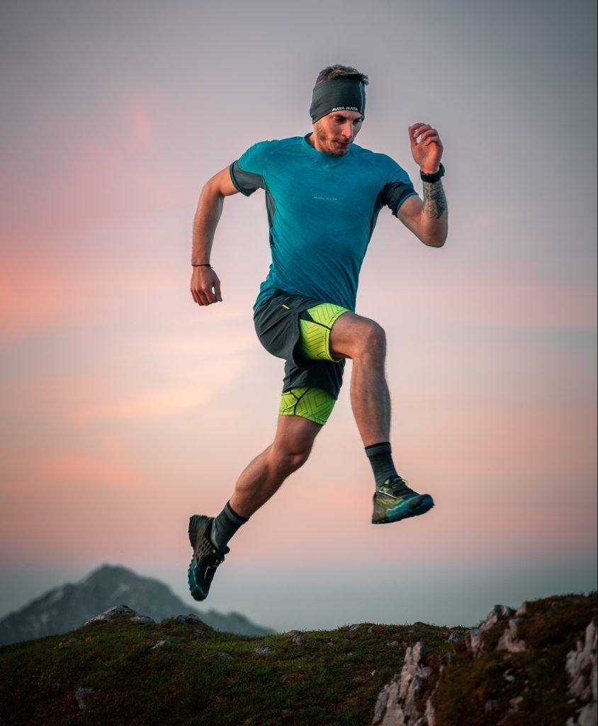 Man jumping on a mountain in the sunset in activewear.